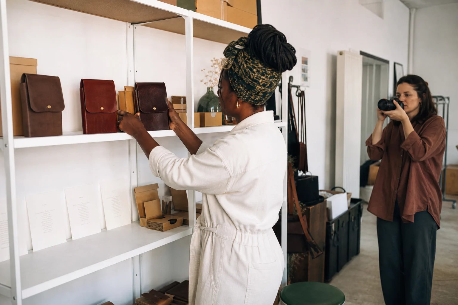 Black leather-goods maker preparing products with a photographer for her website content