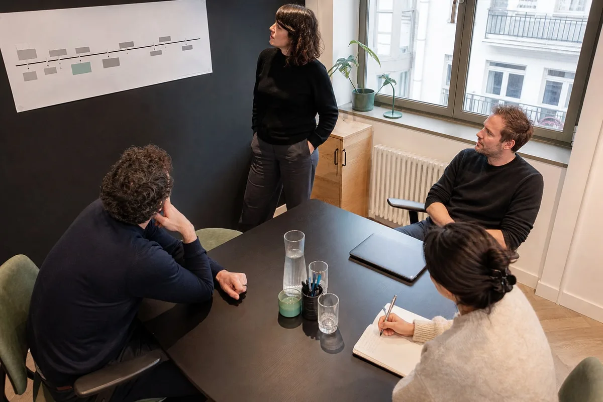 Une équipe autour d'une table de réunion à Bruxelles, planning affiché au mur